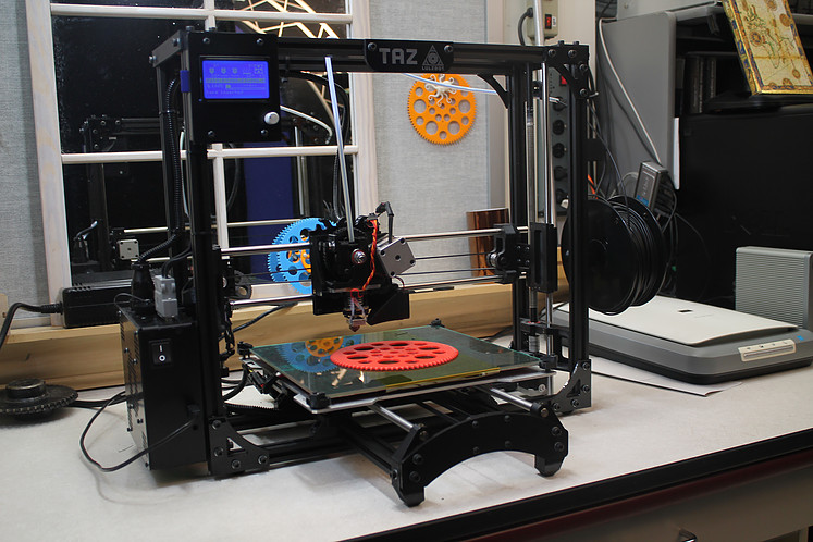 A 3D Printer printing a red gear.