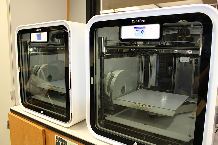 The front glass panels of two large white 3D printers.