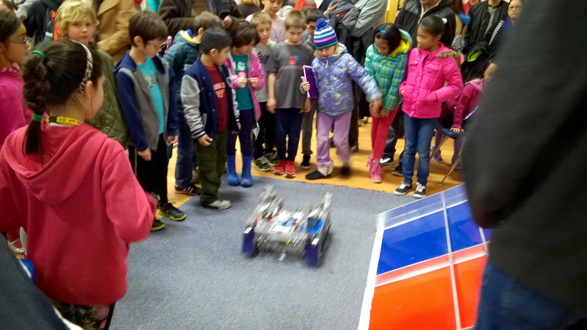 A crowd of children huddle around a robot in the center.