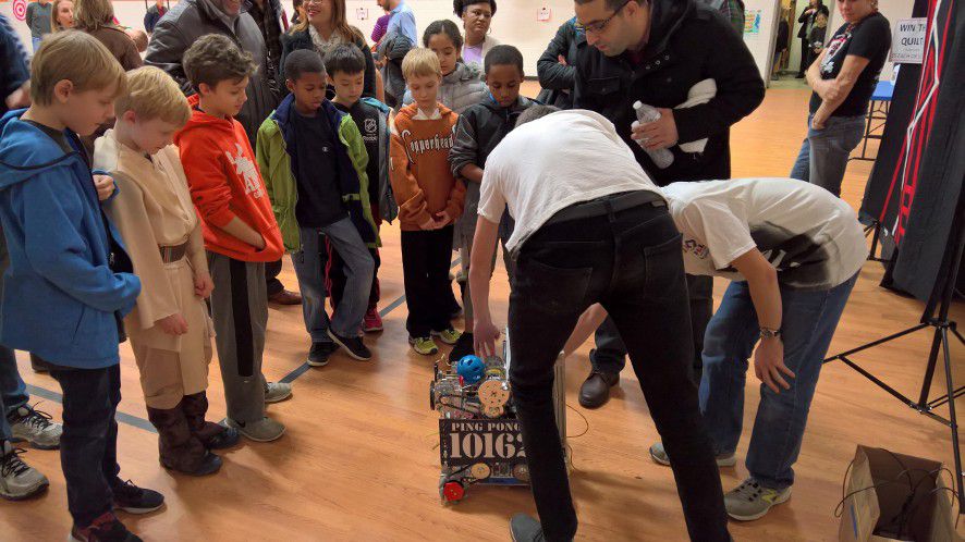 A small crowd of children watching a robot.