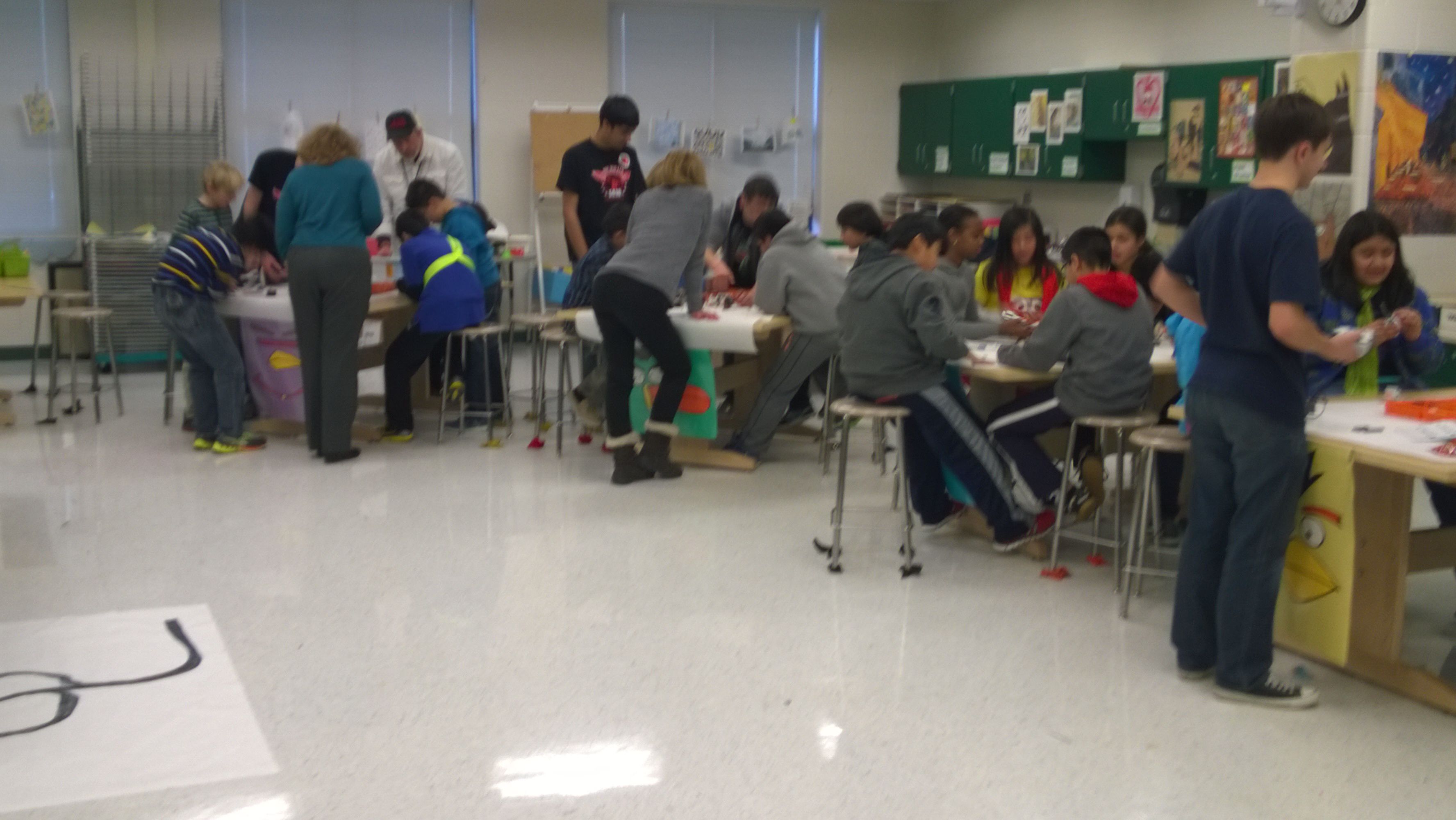 A clean room with tables, where team members and children are building robots.
