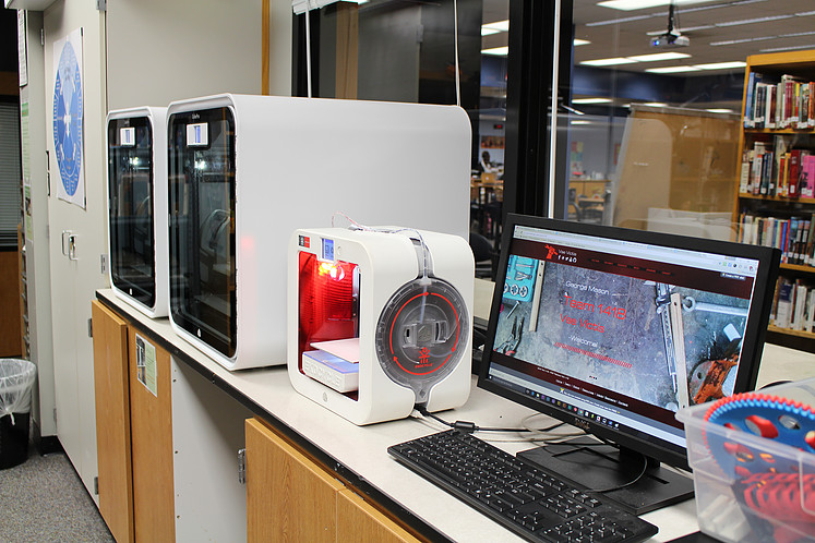 White 3D printers, two large, one small, next to a computer.