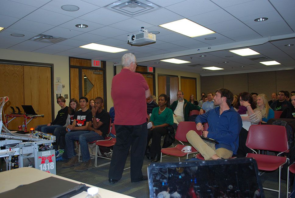 An adult teaching a class to the team and others.