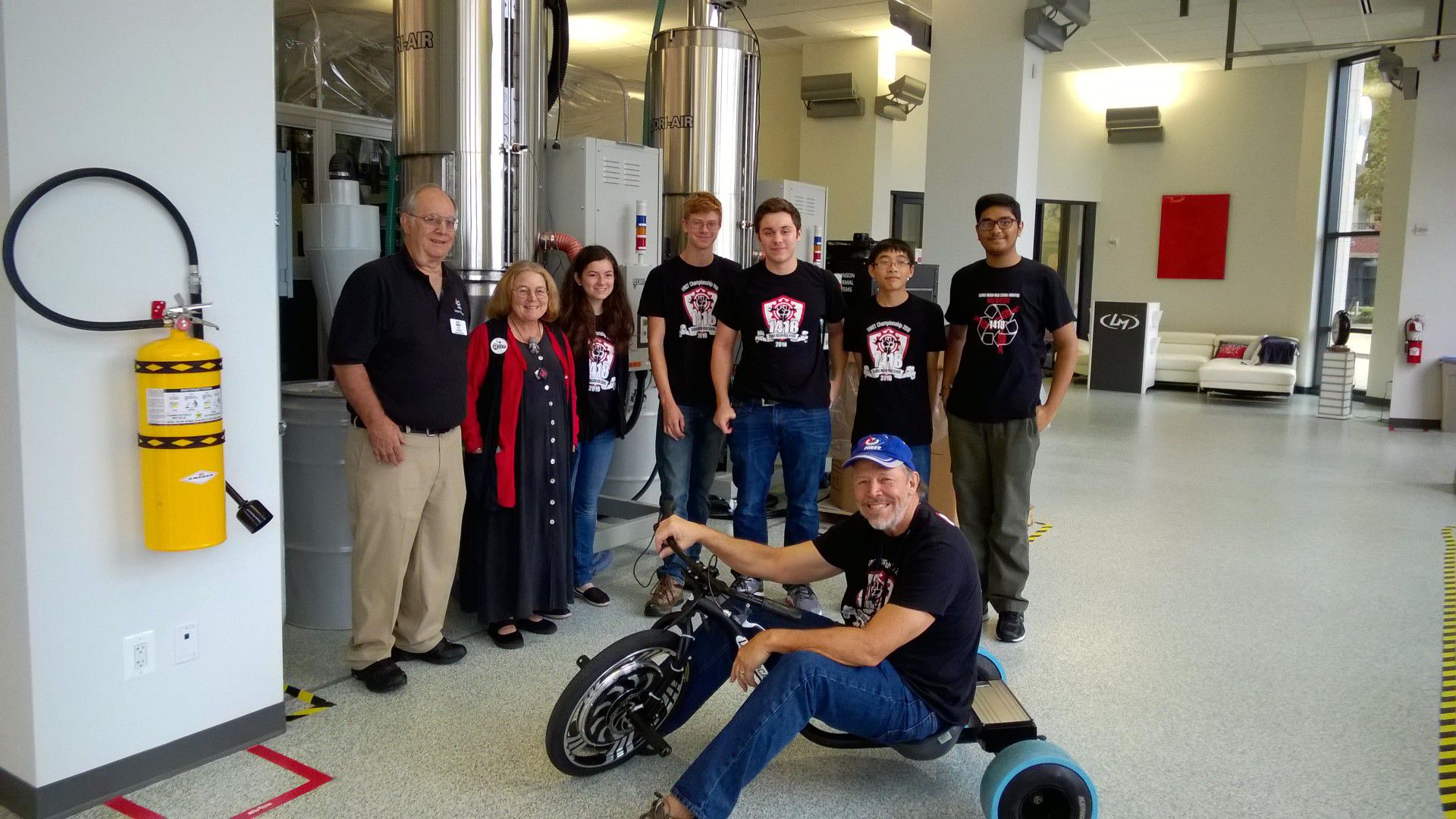 Mr. Ballou smiling on a bike with the team posing in background.