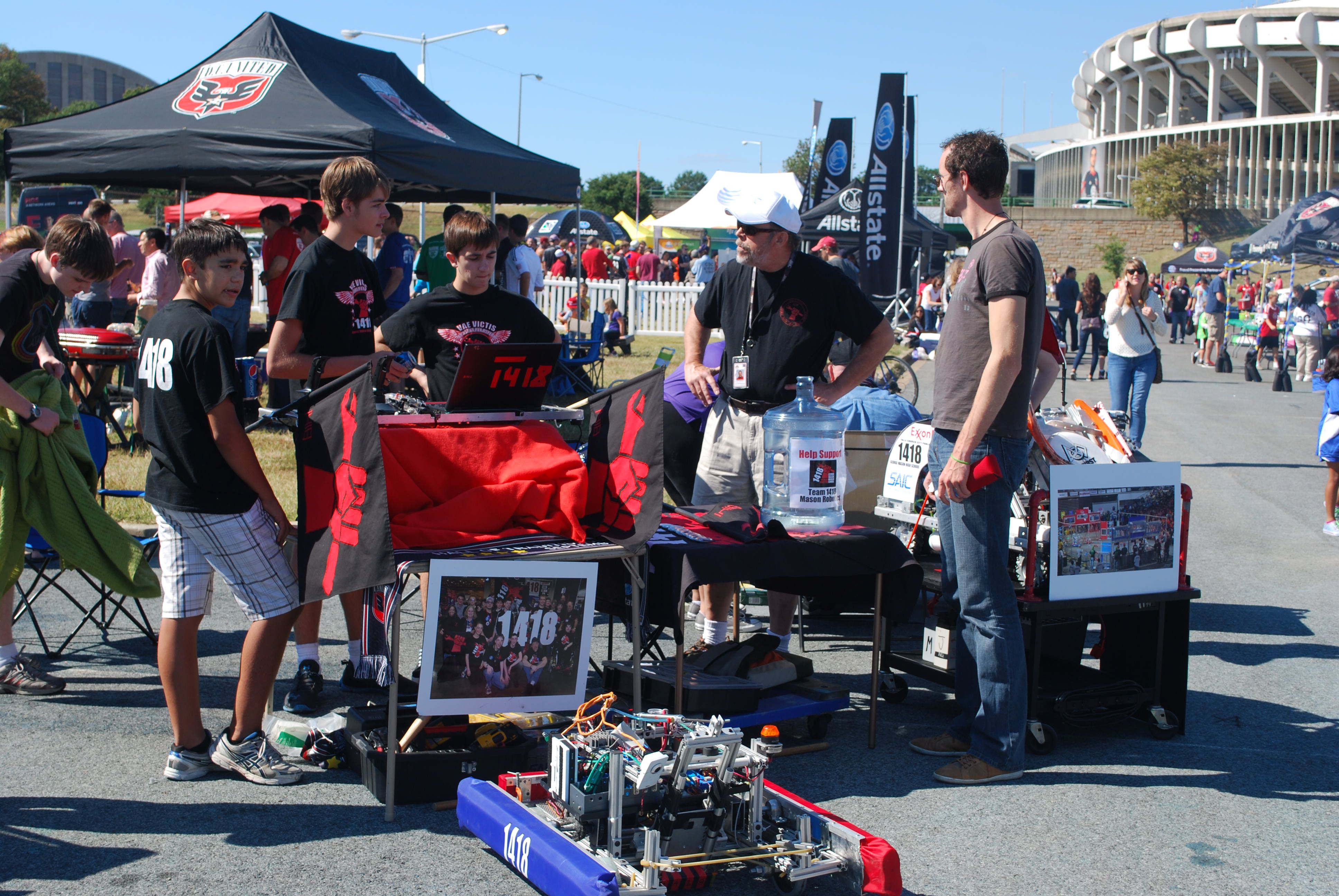 The team talking to an adult at a stand, with the robot in front.